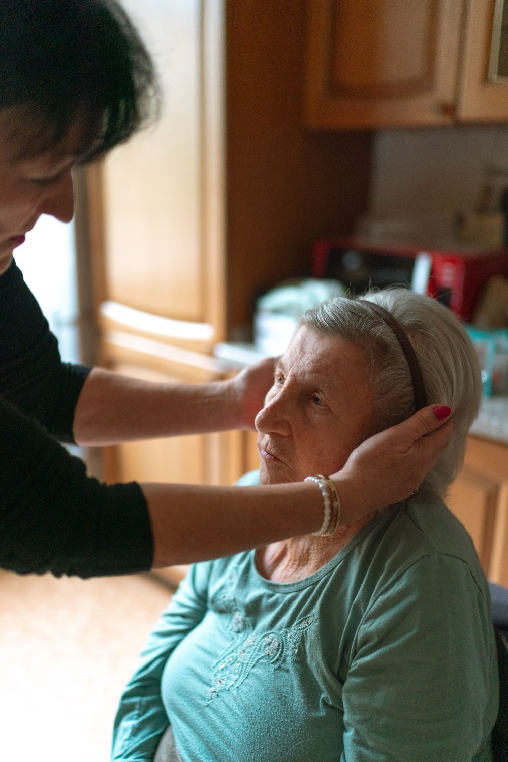 A hospice caregiver gently cradling an older woman's face at home, the two smiling at each other in soft natural light